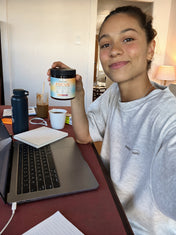 A woman at a desk with a laptop holds up a jar of CappyRoots Focus gummies