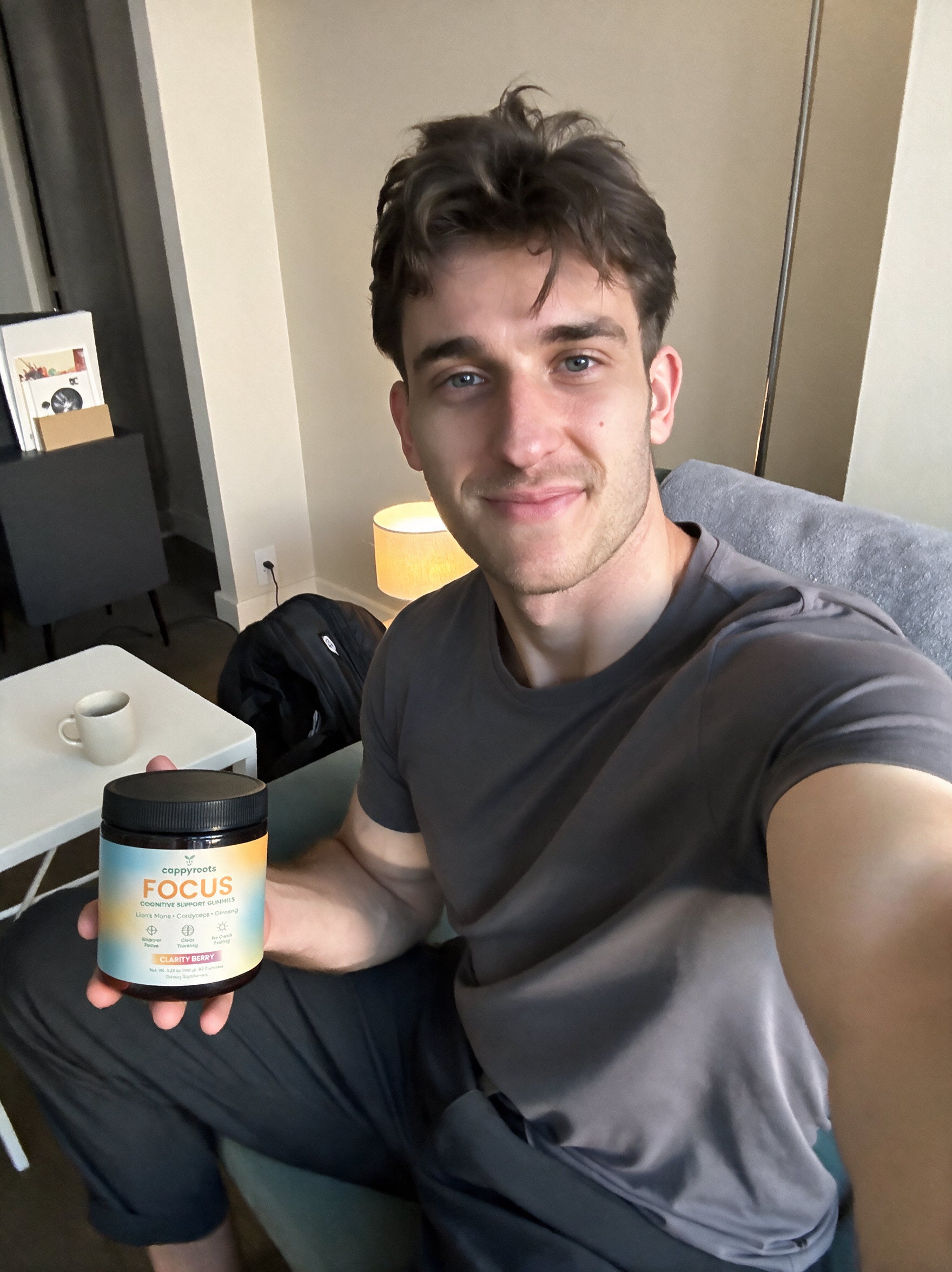 A man in a grey t-shirt sits beside a jar of CappyRoots Focus gummies on a side table
